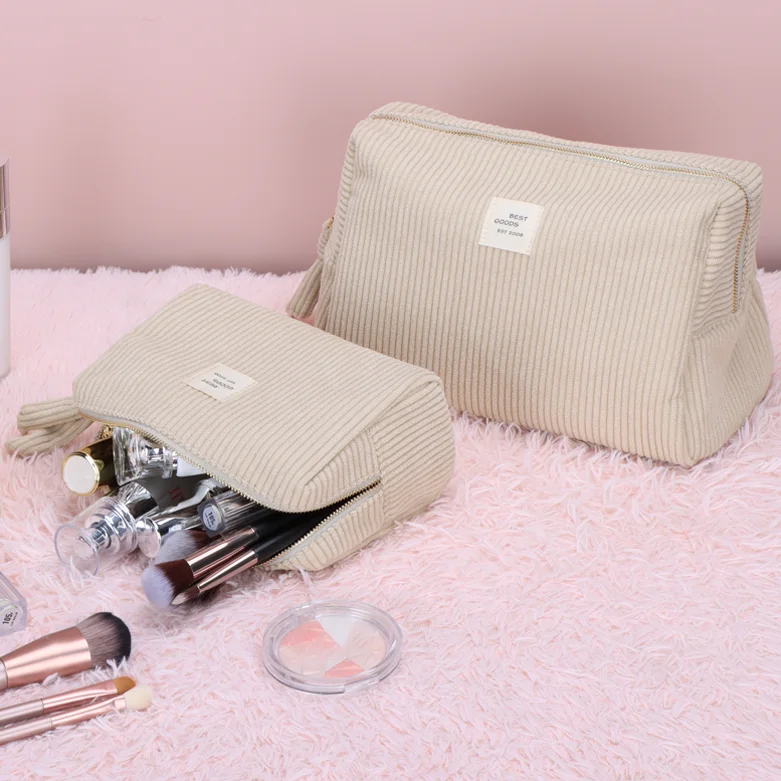 Two cream corduroy zippered cosmetic pouches with woven BEST CHOICE label, one open holding makeup brushes, on a pink shag rug with brushes and a compact
