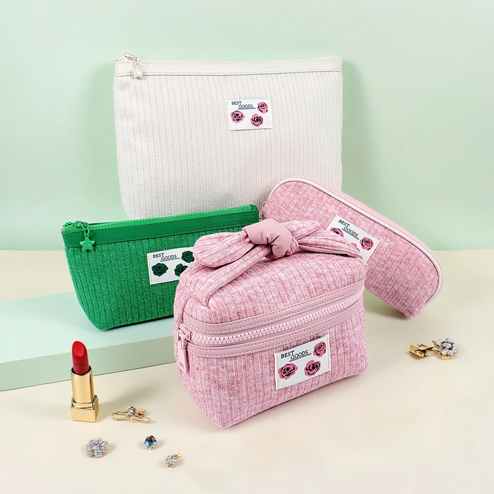Four corduroy cosmetic pouches in ivory, kelly green, and pink with BEST GOODS rose labels, knotted-handle pink case front, styled with gold lipstick and rhinestone earrings on mint backdrop
