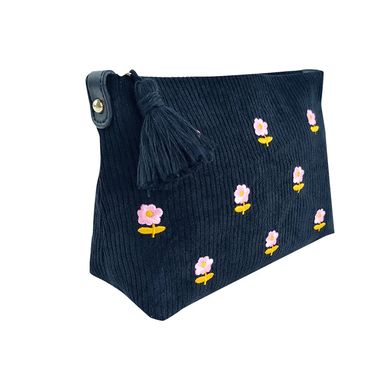 Navy wide-wale corduroy zip pouch with pink daisy embroidery, gold grommet corner tab, and navy tassel pull, isolated on white background