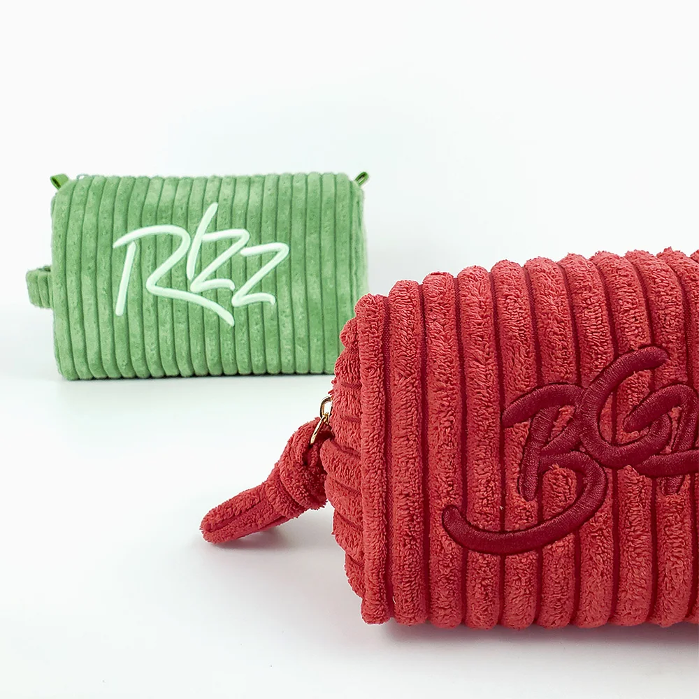 Sage-green and coral-red wide-wale corduroy barrel cosmetic pouches with tone-on-tone script embroidery, styled on a white background
