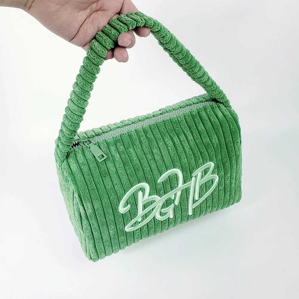 Hand holding sage-green wide-wale corduroy box cosmetic pouch with chunky corduroy top handle and embroidered BGHB script logo, white background