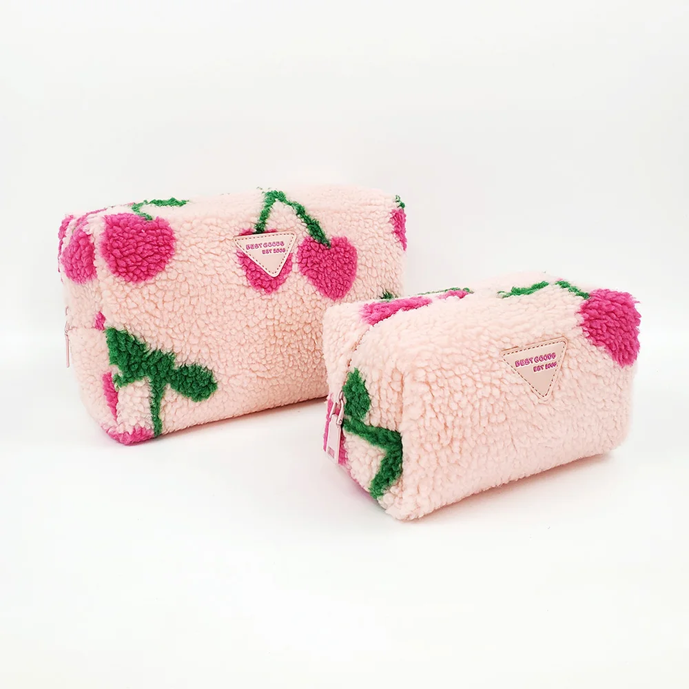 Two blush-pink sherpa cosmetic pouches with tufted magenta cherry motif and triangle BEST GOODS label on white background