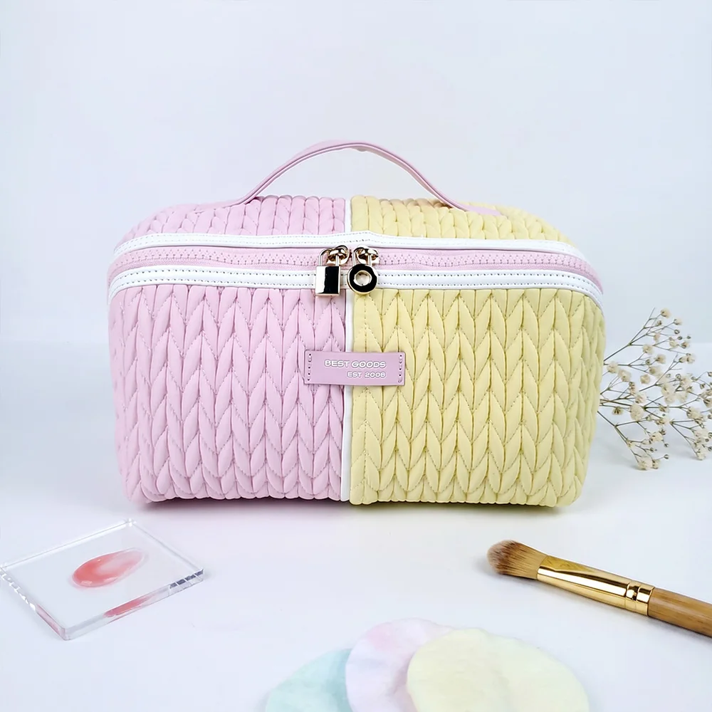 Blush pink and butter yellow braided-texture box cosmetic case with gold zipper pulls and top handle, styled on white with dried flowers and makeup brush