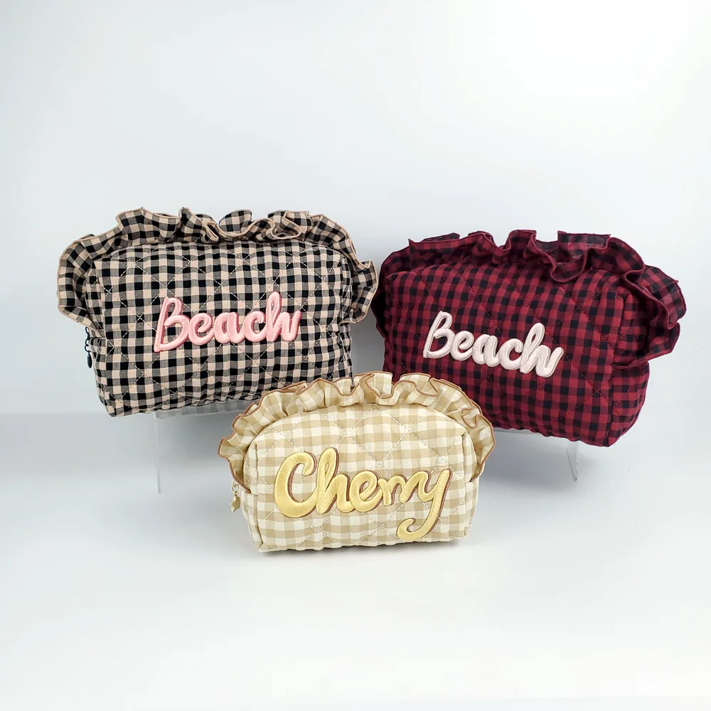 Three quilted gingham ruffle-top pouches in cream-black, burgundy, and tan-cream with raised script lettering 'Beach' and 'Cherry' on white studio background