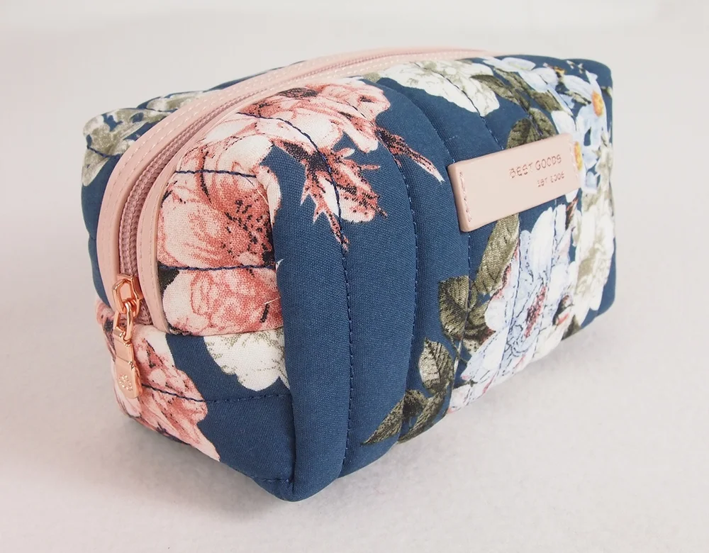 Navy floral-print quilted nylon makeup pouch with blush pink zipper trim and rose-gold pull on white background