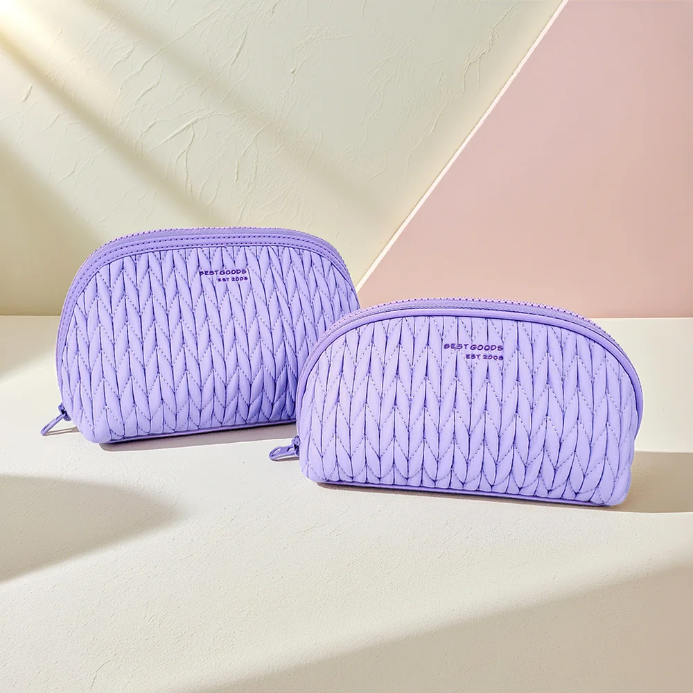 Two lavender quilted dome makeup pouches with chevron stitching and BESTGOODS logo on a cream and pink styled backdrop