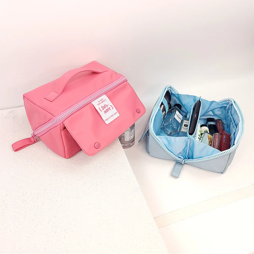 Pink flap-front cosmetic case with top handle beside open blue pouch showing divided interior, styled on white surface
