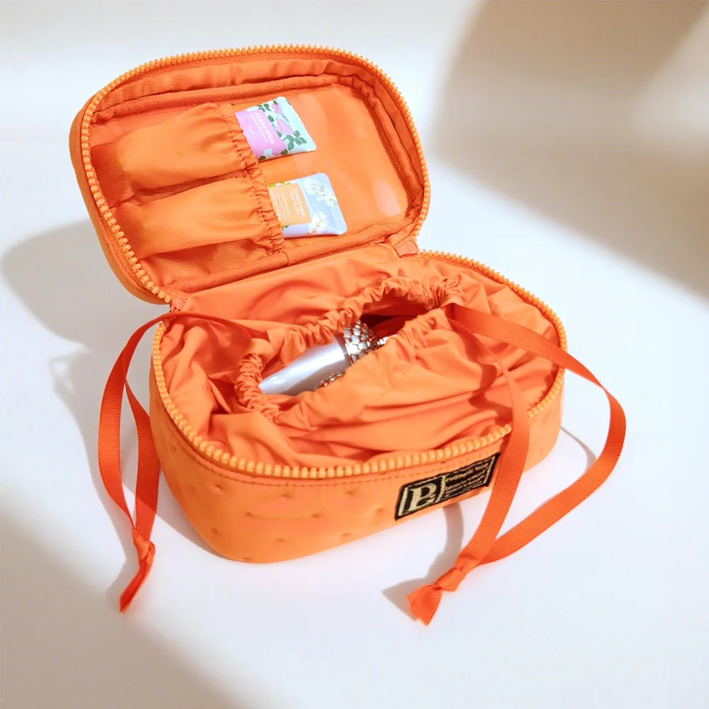 Open tangerine-orange quilted nylon vanity case with drawstring inner pouch, elastic lid pockets and woven P label on light background