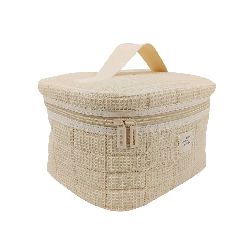 Cream waffle-weave vanity cosmetic bag with top handle and dual zipper pulls on white background