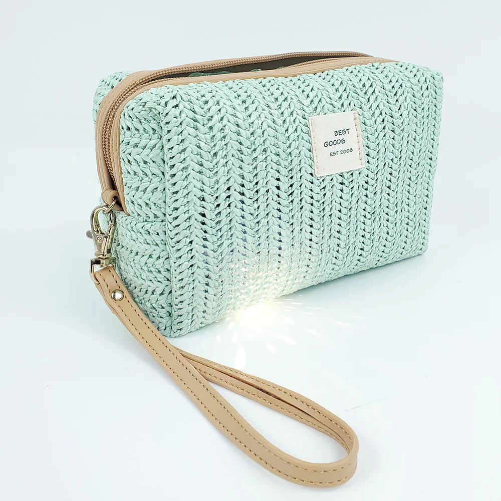 Sage-green woven straw zip pouch with tan trim, gold zipper pulls, and leather wrist strap on white background
