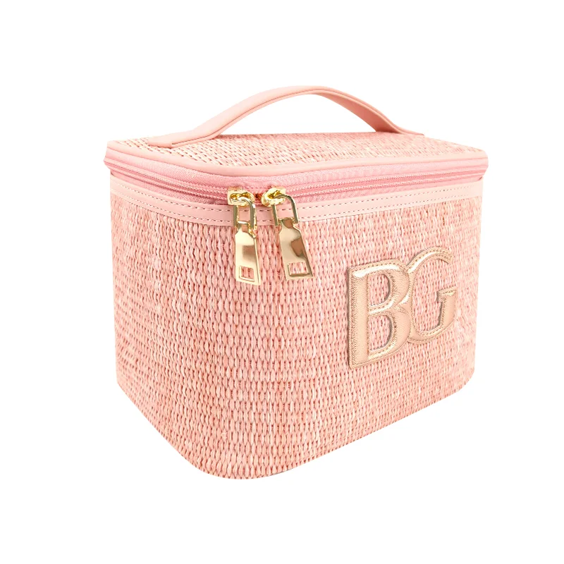 Blush-pink woven straw vanity case with pink top handle, gold dual zipper pulls, and metallic gold BG monogram on white background
