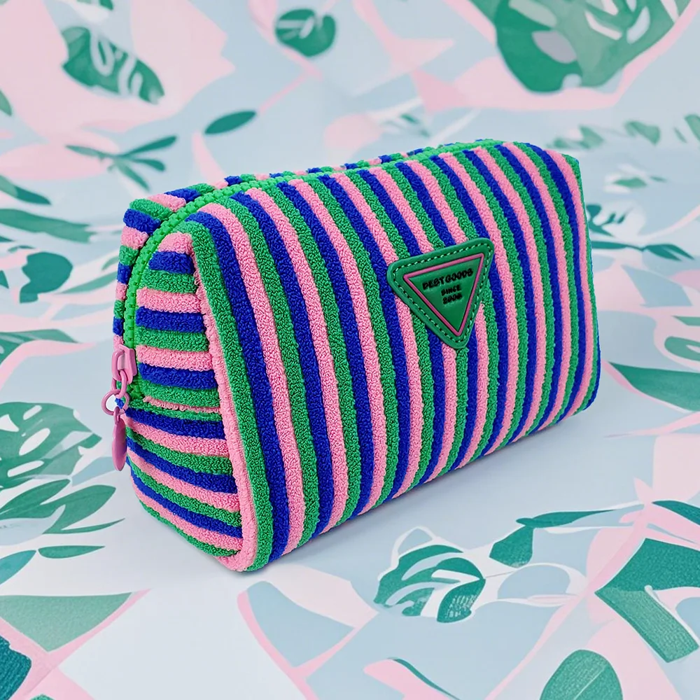 Striped terry cloth cosmetic pouch in pink, green, and cobalt blue with green triangle patch, on tropical leaf print background
