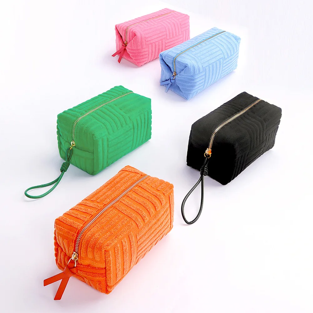 Five boxy basketweave terrycloth zip pouches in pink, sky-blue, green, black, and orange with gold zippers and ribbon pulls arranged on a white background